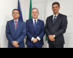 Fundo de parede na cor branca. À frente, 3 homens de terno no tom escuro posam para a foto