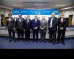 Homens posando para foto, vestidos com ternos, em uma sala de auditório.