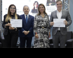 Foto de duas mulheres e dois homens em pé. Estão num auditório e uma das mulheres e um dos homens seguram um certificado.