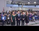 Foto de duas mulheres e dois homens de pé, à frente de uma plateia em auditório. Os quatro estão de costas para a plateia, posando para a foto.