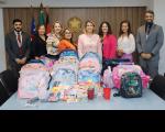 Grupo de oito pessoas posando para foto, atrás de uma mesa repleta de mochilas, com o brasão da República ao fundo.