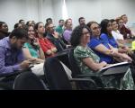 Foto de grupo de pessoas em plateia, assistindo à palestra. Ao fundo, parede branca.