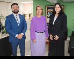 Três pessoas posando para foto dentro de uma sala. Um homem e duas mulheres.