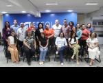 Grupo de pessoas posando para uma foto dentro de um auditório. Parte das pessoas estão em pé, lado a lado, e outra parte estão sentadas em cadeiras de cor preta.