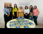 Sete pessoas em pé, atrás de uma mesa redonda, posando para foto. Sobre a mesa, cartilhas espalhadas.
