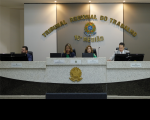 Foto de dois homens e duas mulheres sentados em uma bancada com computadores e microfones à sua frente. Ao fundo, parede listrada em branco e marrom, com o nome do TRT-16 em letras douradas, tendo abaixo o brasão da República. Na base da foto, vê-se a frente da bancada em mármore preto e branco com o brasão da República centralizado, todo em dourado.