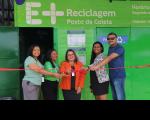 Foto mostra cinco pessoas em pé, fazendo o corte de uma fita inaugural. Ao fundo um painel verde com informações em letras brancas: E + RECICLAGEM. Posto de Coleta.