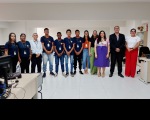 Foto de doze pessoas, entre jovens e servidores do TRT-16, de pé e sorrindo. Atrás deles, parede clara. Nas laterais, móveis de escritório em tons de bege.