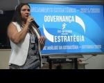 Foto de uma mulher falando ao microfone. Ao fundo um painel azul com letras brancas: Planejamento Estratégico 2021/2026. Governança Estratégica
