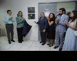 Foto mostra um grupo de pessoas em pé, ao lado de uma placa de inauguração. Uma mulher e um homem seguram um tecido azul.