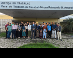 Foto mostra um grupo de pessoas posicionadas em pé na frente de um prédio. Na parte superior um letreiro: JUSTIÇA DO TRABALHO - VARA DO TRABALHO DE BACABAL