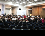 Foto mostra várias pessoas em pé, no palco de um auditório