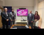 Foto mostra 3 homens e uma mulher. Todos estão em pé na frente de um monitor de tv com a informação audiência pública