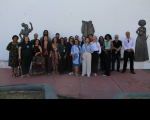 Foto mostra várias pessoas reunidas sobre uma calçada. Ao fundo uma parede branca. E três estátuas refentes a cultura Afro