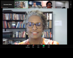 Foto mostra um print de uma transmissão na internet. Ao centro aparece um rosto de uma mulher negra. Ela tem cabelos cursos e está sorrindo