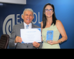Foto mostra um homem e uma mulher, segurando um certificado e uma placa de homenagens.