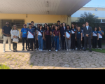 Foto mostra várias pessoas reunidas em frente a um prédio. Elas estão posicionadas um ao lado da outra.