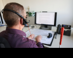 Foto de um homem PCD de costas, utilizando um notebook e fones de ouvido.