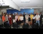Foto mostra várias pessoas em pé, dentro de um auditório. Ao fundo, parede azul.