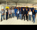 Foto mostra um grupo de pessoas em pé, olhando para a frente. Todos estão em um salão