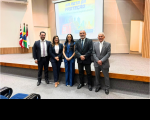 Foto mostra cinco pessoas em pé, uma ao lado da outra dentro de um auditório