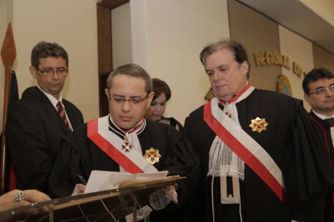 dois homens de toga em pé, estando um na tribuna assinando termo de posse e o outro ao lado
