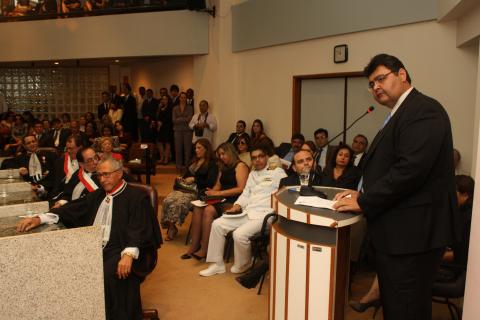 Homem de terno, em pé, em frente a um tribuna discursando