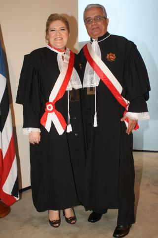 Mulher ao lado de um homem, ambos de toga pousando para foto. 