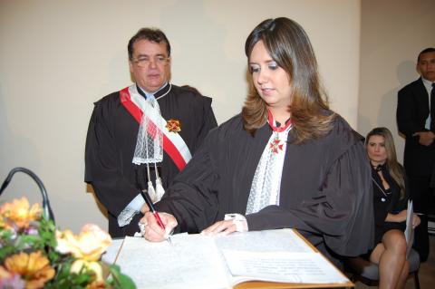 Mulher de toga em pé, atrás de uma tribunal, assinando o ato de posse 