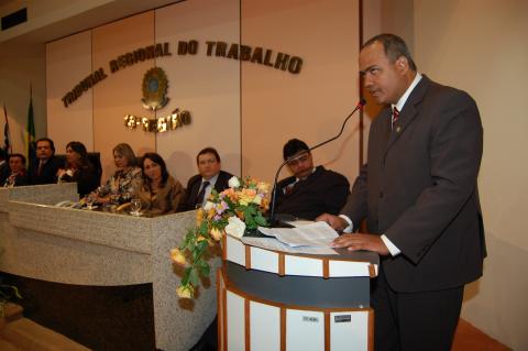 Homem de terno, em pé, em frente a um tribuna discursando