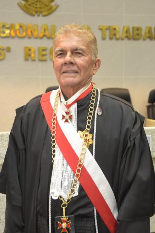 Homem de toga em pé com uma faixa branca e vermelha 