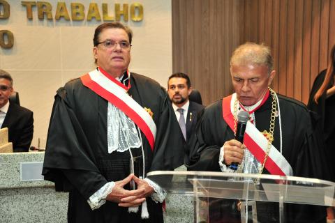 dois homens de toga em pé, estando um na tribuna lendo termo de posse e o outro ao lado