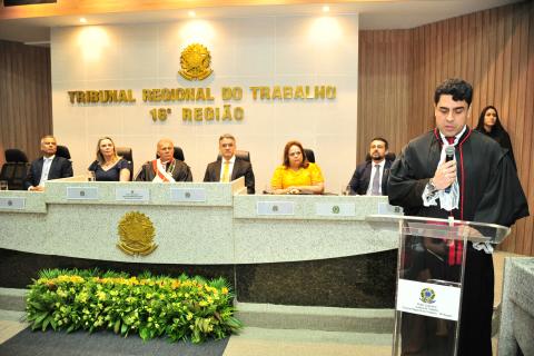 Homem de toga, em pé, em frente a um tribuna discursando