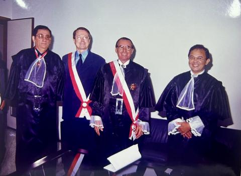 Três homens de toga preta e um de terno, todos em pé pousando para foto