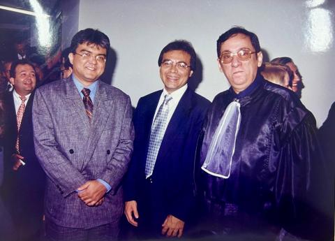 Dois homens de de terno e um de toga preta, todos em pé, pousando para foto